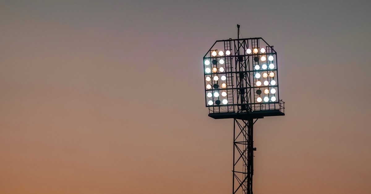 Stadium floodlights switched on against an orange evening sky