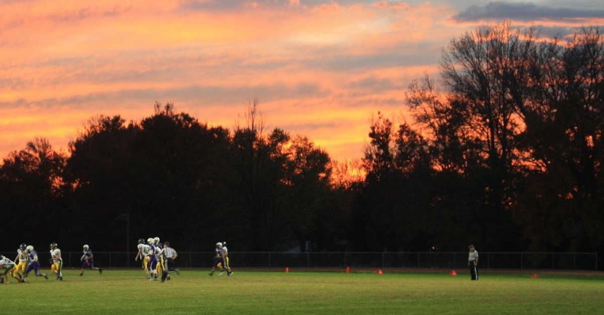 Football players on a grass field at sunset with dark trees behind them