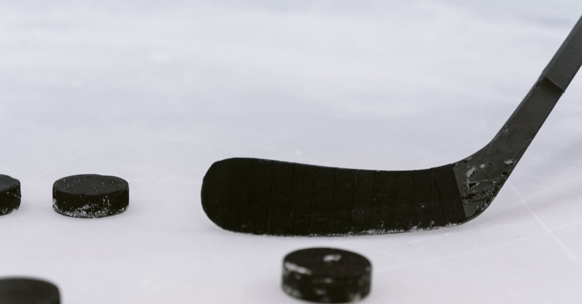 A hockey stick blade and three pucks resting on white ice