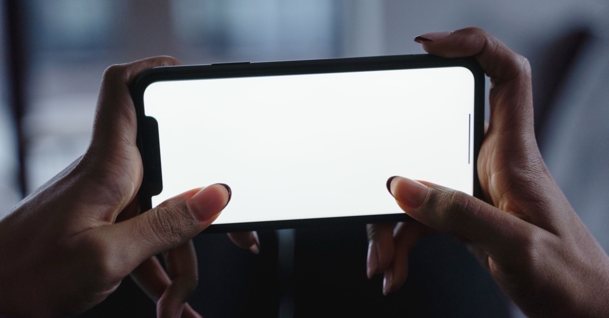 Two hands holding a smartphone sideways with a blank, glowing screen